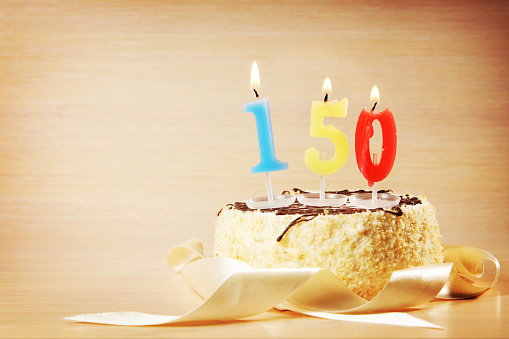 Birthday cake with burning candle as a number one hundred and fifty. Focus on the candle