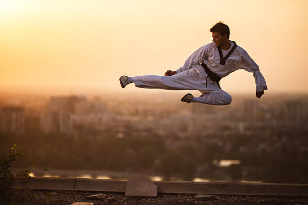 Skillful martial artist exercising at sunset and performing jump kick while being in fly kick pose.