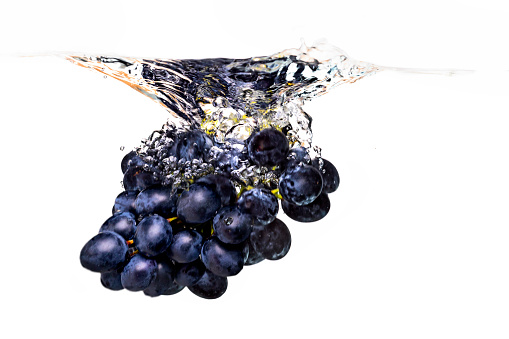 Blue grape dropped into water with splash isolated on white