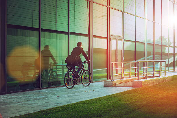 Handsome man riding bicycle beside the modern office building Rear view of a handsome man, on the way to work, riding bicycle beside the modern office building. The man is casually dressed and wears eyeglasses and carries black briefcase hung on shoulder. Blurred motion, copy space has been left. portability stock pictures, royalty-free photos & images