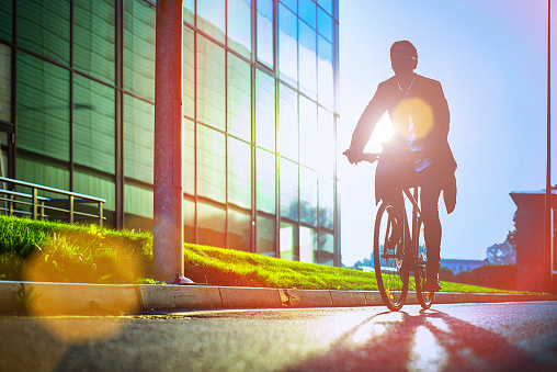 Handsome man, on the way to work, riding bicycle beside the modern office building. The man is casually dressed and wears eyeglasses and carries black briefcase hung on shoulder. Blurred motion, copy space has been left.