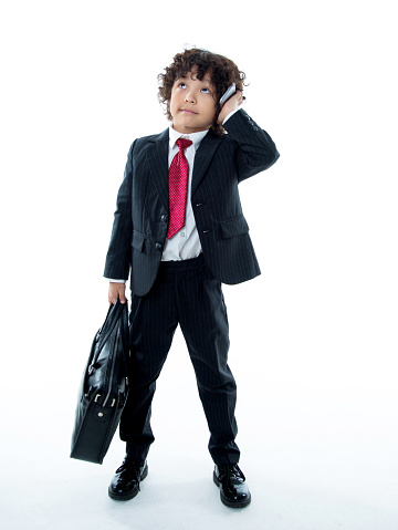 Young boy dressed like businessman talking on the phone against white background.