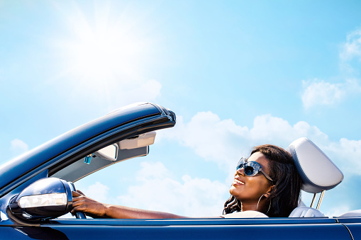 Close up portrait of attractive elegant african woman driving convertible under sunny sky.
