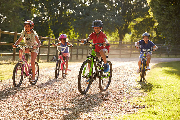 cuatro niños en un paseo en bicicleta en el campo juntos - bicicleta de carreras fotografías e imágenes de stock