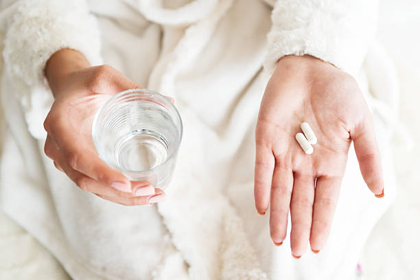 mulher segurando um copo de água e pílulas, detalhe - capsule vitamin pill pill nutritional supplement - fotografias e filmes do acervo