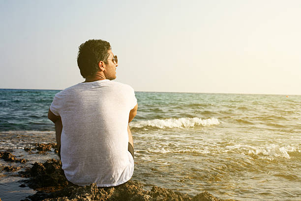Arabian man sitting on coastline. Space for copy.
