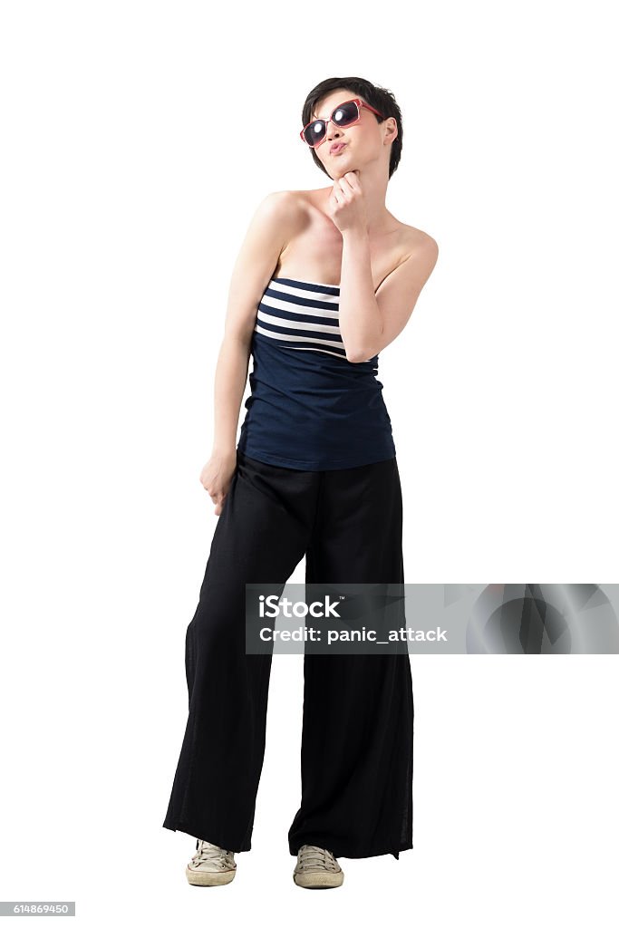 Young flirty short hair beauty with sunglasses blowing a kiss. Young flirty short hair trendy beauty with sunglasses blowing a kiss. Full body length portrait isolated over white studio background. Wide Leg Pants Stock Photo
