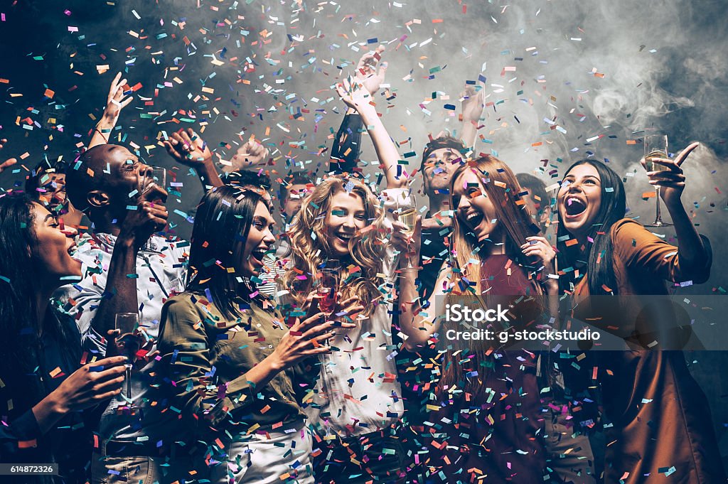 Fun in motion. Group of beautiful young people throwing colorful confetti while dancing and looking happy Party - Social Event Stock Photo