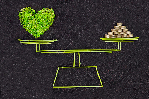 A measuring scale measuring a green heart and a pile of golden coins / Business ethics / Moral behavior in business / Corporate social responsibility / Weighing nature and economy