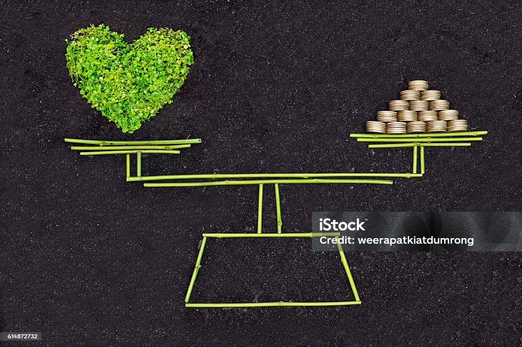 Business ethics A measuring scale measuring a green heart and a pile of golden coins / Business ethics / Moral behavior in business / Corporate social responsibility / Weighing nature and economy Currency Stock Photo