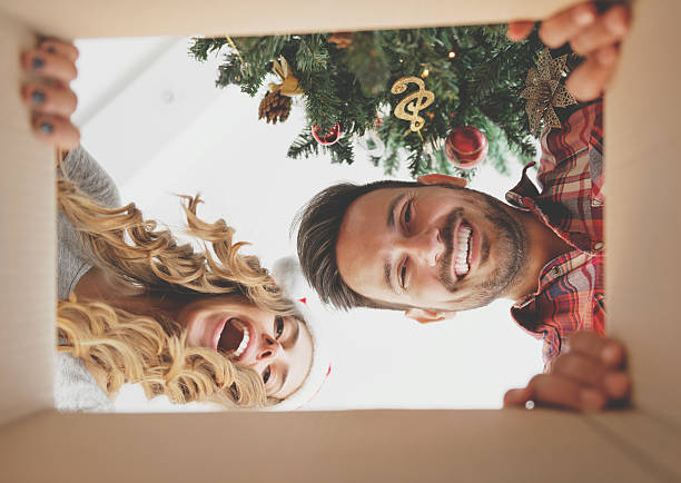 young couple opening a christmas present - prenda de natal fotos imagens e fotografias de stock