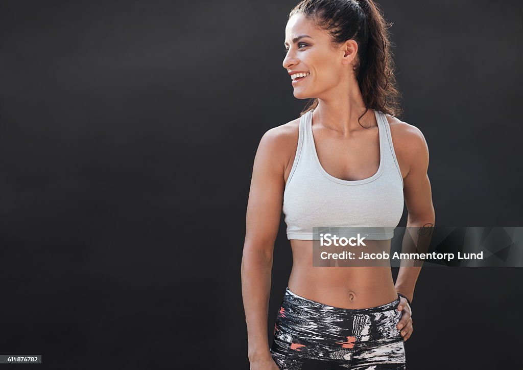 Happy young woman in sports clothing smiling Happy young woman in sports clothing smiling. Muscular fitness model on black background looking away at copy space. Women Stock Photo