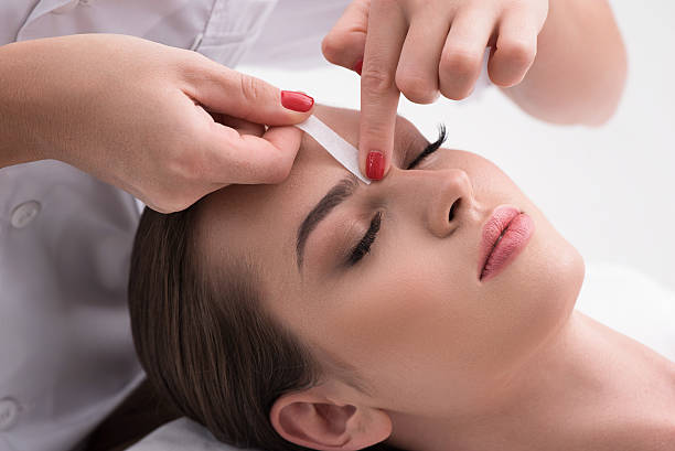 Young woman tweezing her eyebrows in beauty saloon Already perfect. Close up of hands waxing beautiful woman eyebrow, lying in beauty salon with closed eyes isolated on white background wax stock pictures, royalty-free photos & images