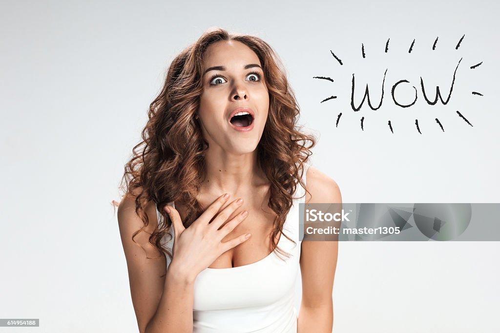 Portrait of young woman with shocked facial expression Portrait of young woman with shocked facial expression  over gray background Surprise Stock Photo