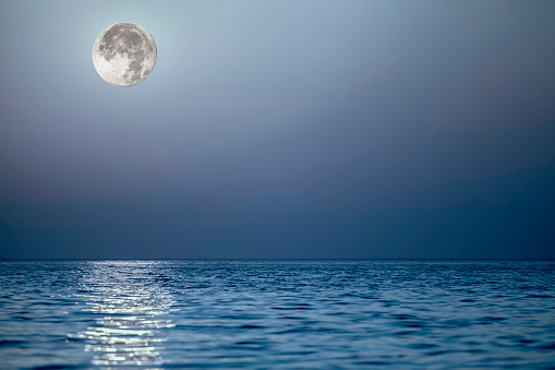 Light from the moon reflecting off a calm blue sea at the horizon. Serene composite image with natural copy space.