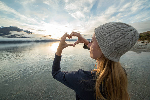 istock Young woman by the lake makes heart shape finger frame 614957664