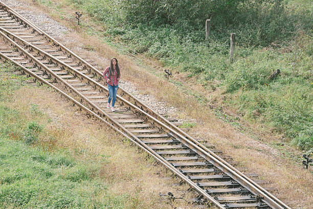 Girl with backpack walking down the railroad track. High angle isometric view. Photo is taken with dslr camera and telephoto lens outdoors.