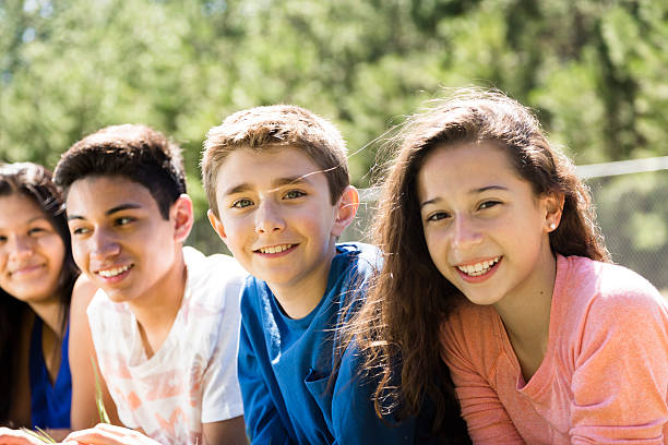 Group of teenage friends at local park or school campus. Multi-ethnic group of teenage friends hang out together at a local park or school campus setting.  Spring or summer season. happy young teens stock pictures, royalty-free photos & images