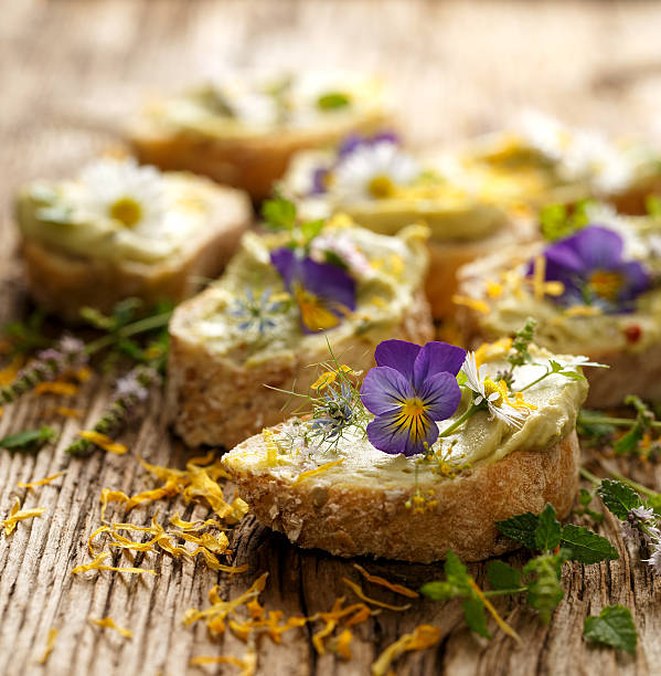 Canapes with eddible flowers and broad bean hummus Canapes with eddible flowers and broad bean hummus on a wooden table edible flower stock pictures, royalty-free photos & images