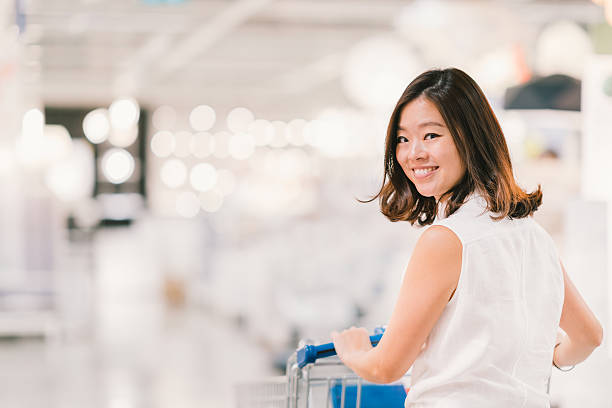 hermosa mujer asiática sonriendo, con carrito de compras - department store shopping teenage girls clothing fotografías e imágenes de stock