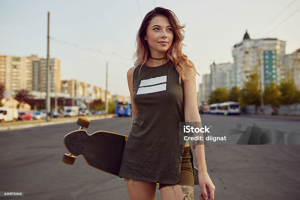 Beautiful young tattooed girl with longboard in sunny weather Beautiful young tattooed woman with his longboard on the road in the city in sunny weather Teenage Girls Stock Photo