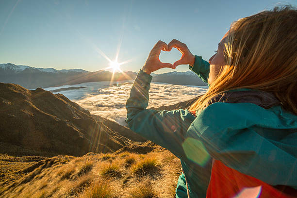 istock Woman on mountain top makes heart shape frame to landscape 614973498