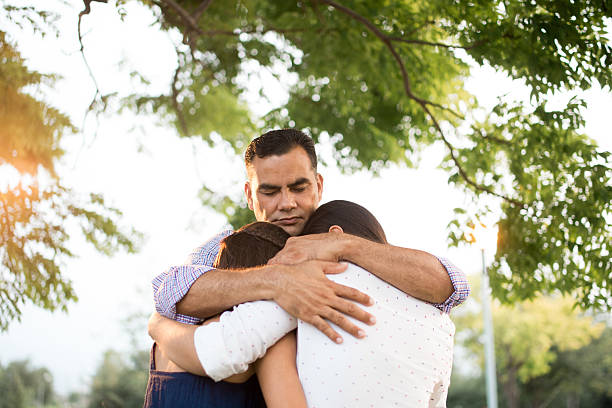 Latin father and daughters embracing in circle A latin father embracing his daughters in circle in a horizontal waist up shot outdoors. face down stock pictures, royalty-free photos & images