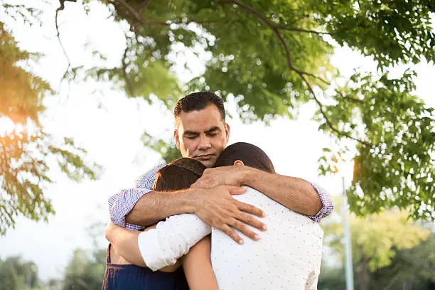 Photo of Latin father and daughters embracing in circle