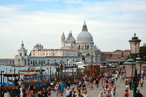 Venice, Veneto, Italy - September 5, 2016: View from the waterfront Riva degli Schiavoni with tourists at the Basilica Santa Maria della Salute with the Punta della Dogana of Venice in Italy.