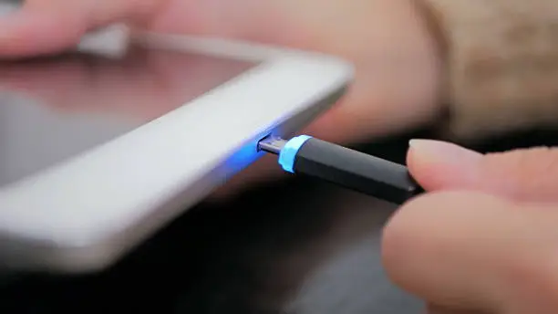 Woman's hand plugging black lightning charging cable into pc digital tablet - USB data cable connecting on modern gadget. Close up