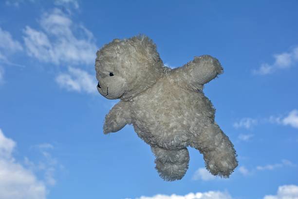 White Teddy bear flies in the air with blue sky with clouds