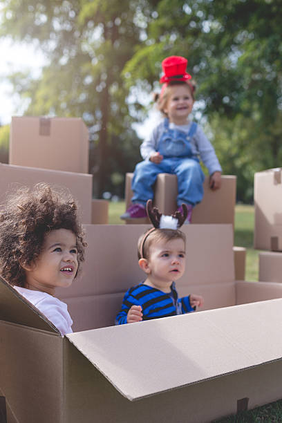 three multi ethnic babies playing outside mixed race , baby , park , outside , birthday , new year , celebration , party , transportation , cardboard boxes cardboard box fort stock pictures, royalty-free photos & images