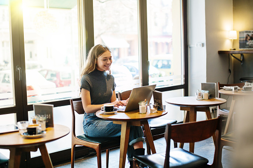 Happy young woman sitting at a cafe and surfing internet on her laptop