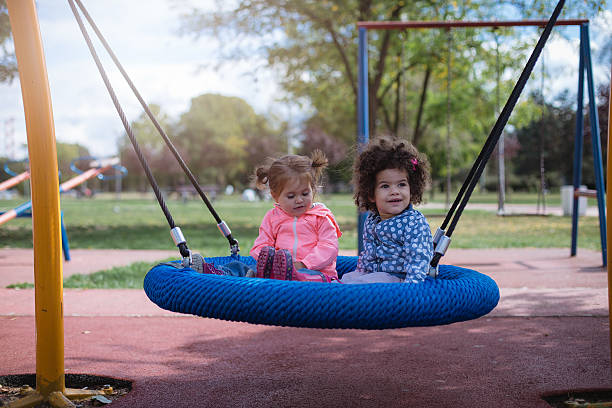 zwei multikulturelle babys spielen auf einer schaukel im park - playground cute baby blue stock-fotos und bilder