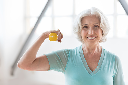 Healthy lifestyle. Delighted good looking enthusiastic woman holding a small yellow rubber dumbbell and smiling while looking at you