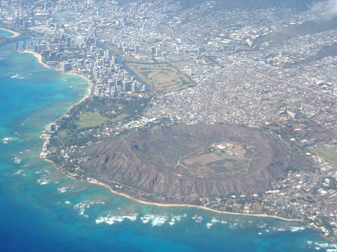 Aerial of Diamond Head Crater, Waikiki, and Honolulu with wave bracking against reef on nice day.