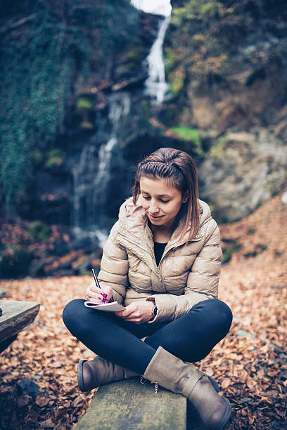 istock Young Relaxed Woman how Writing by the Waterfall in Autumn 615077660
