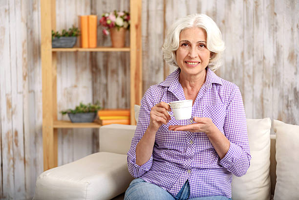 istock Happy old lady drinking hot beverage at home 615077858