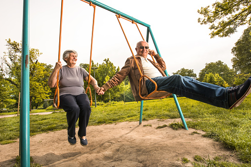 Happy old couple having fun in the park while holding hands and swinging.