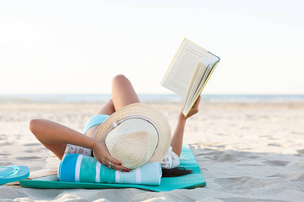 женщина читает книгу во время принятия солнечных ванн на пляже - beach beauty in nature beautiful brown hair стоковые фото и изображения