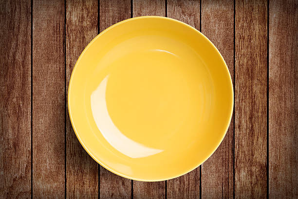 istock Simple yellow circular porcelain plate on wood with clipping path 615087296