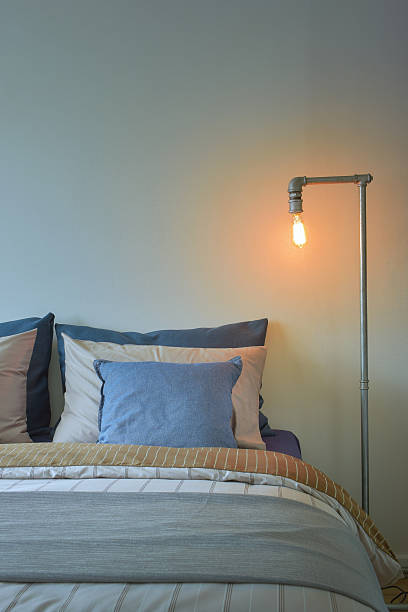 istock Industrial style reading lamp and blue pillows on bed 615088868