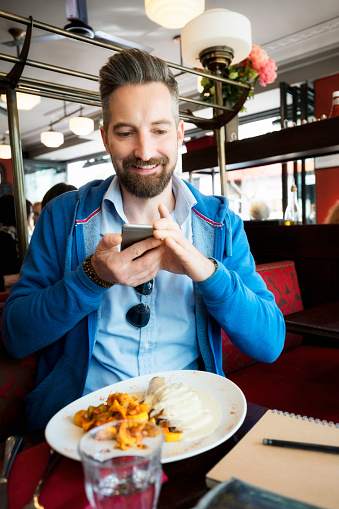 Smiling man photographing food while sitting at restaurant