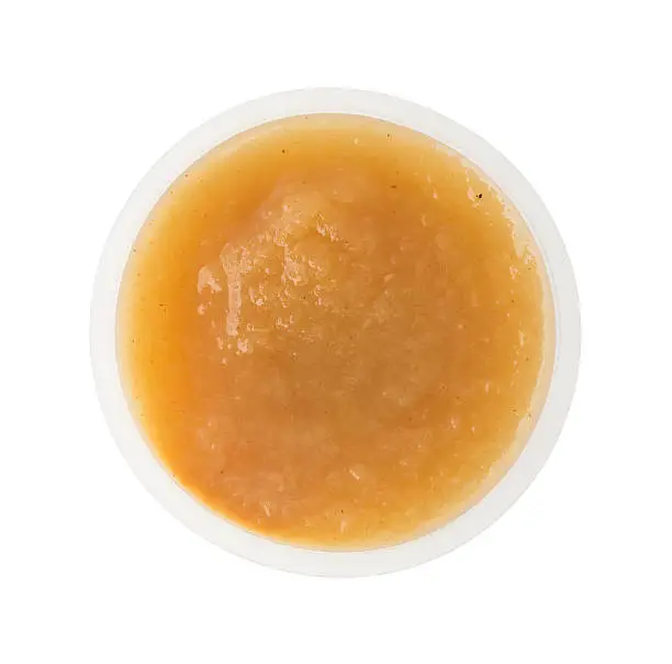 Top view of a serving of organic cinnamon applesauce in a small plastic container isolated on a white background.