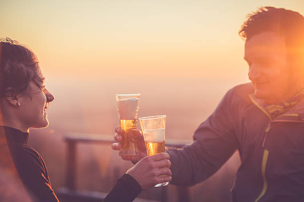 Happy Couple Drinking Beer after Cross-Country Running, Alps, Autumn, Europe Happy young woman and man drinking beer after running uphill on the mountain Sabotin in Julian Alps, Slovenia-Italy border, Europe. They are holding their glasses and toasting.  Autumnal colors, golden hour.  Nikon D800, full frame, XXXL. golden hour drink stock pictures, royalty-free photos & images