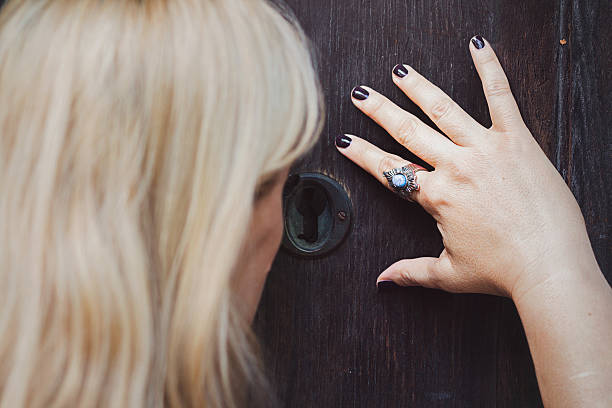 Blonde woman looking thru keyhole Beautiful blonde woman looking thru keyhole on an old wooden door woman spying through a keyhole stock pictures, royalty-free photos & images
