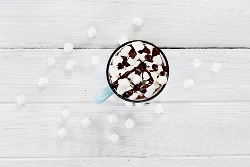 Overhead view of a cup of hot chocolate with marshmallows drizzled with chocolate sauce.