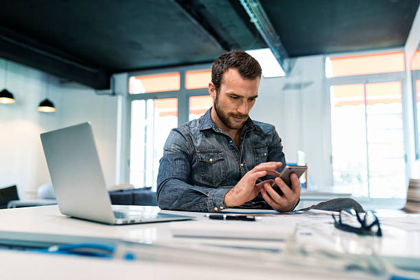 Man using a app mobile phone in modern office start-up. Young male in modern office start-up working on laptop. using smartphone. Sms, message, chat, texting text photography stock pictures, royalty-free photos & images