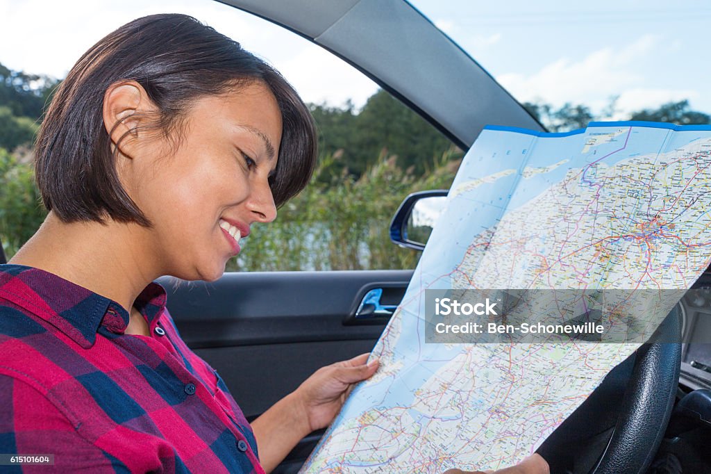 Woman reading road map in car outdoors European woman reading road map in car outdoors. The dutch person is looking at the country map of the netherlands to symbolize that she's traveling and planning a route or course to reach her destination by car. As a driver she has a driving license and this vehicle is a common means of transport. Concept of travel, vacation, holidays, pleasure,  plan, roads, road, street, streets, area, environment, seek, lost, aim,target, ride, on the way. 30-34 Years Stock Photo