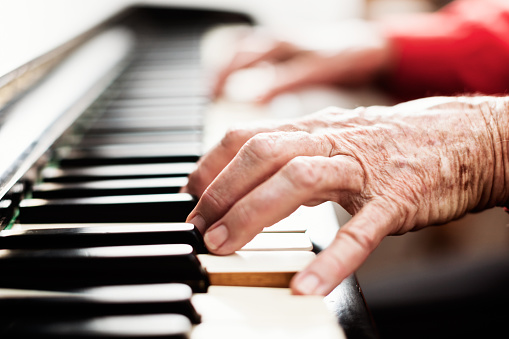 Brightly lit, a pair of old, arthritic, wrinkled hands play the piano.